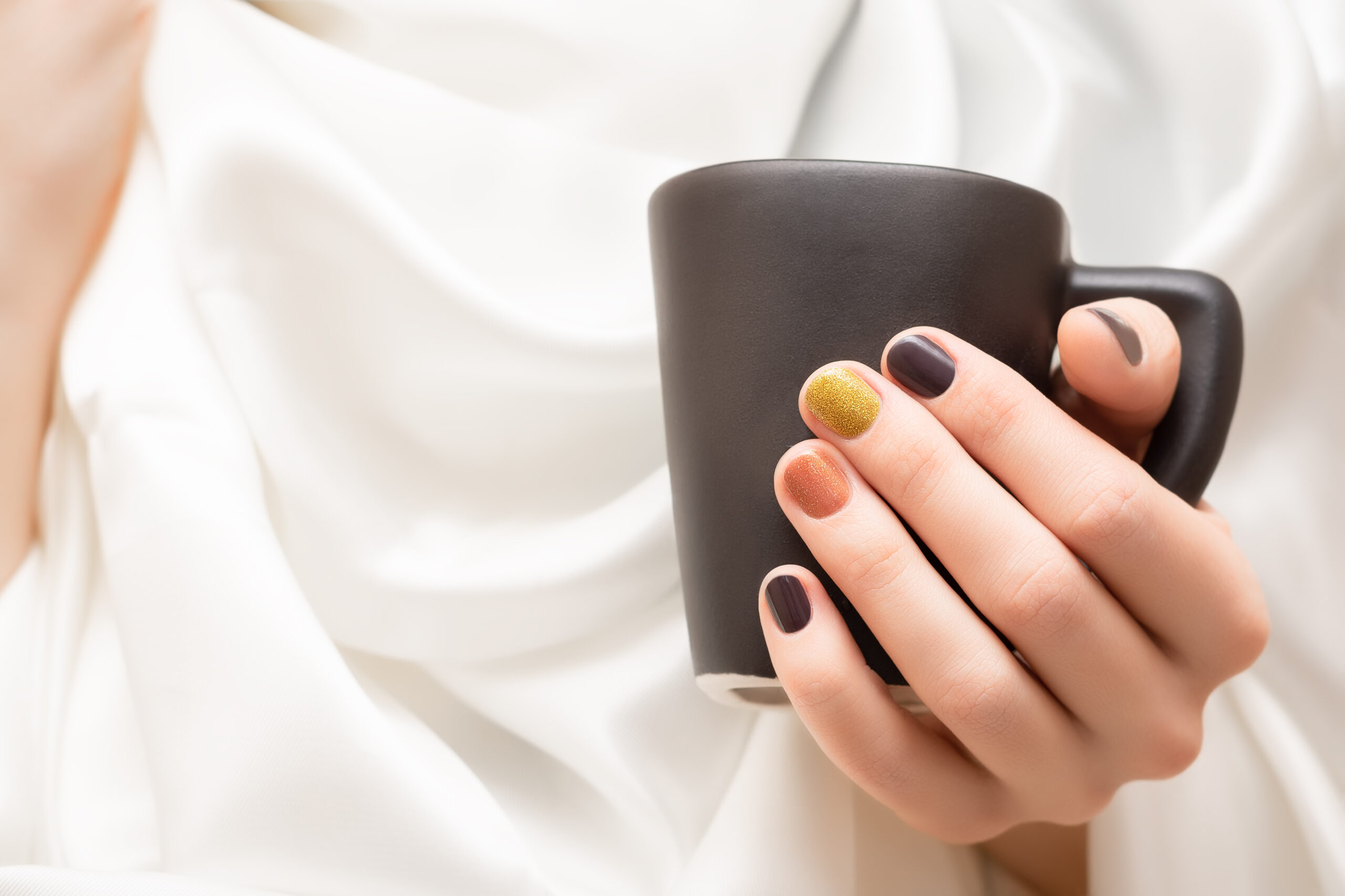 Female Hand With Brown Nail Design Holding Black Cup